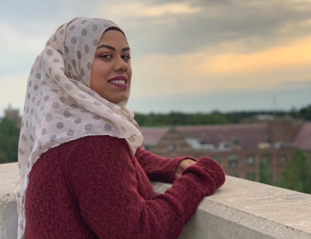 woman wearing a burgundy sweater and a headscarf looking out to a city