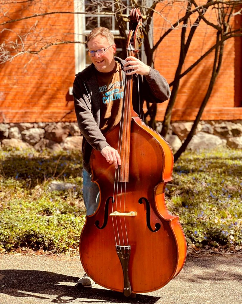 Man standing outside playing a bass instrument. 