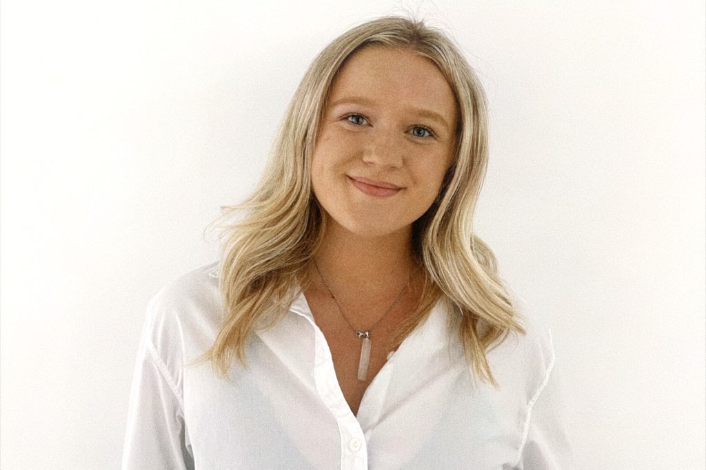 A picture of a woman in a white shirt with a silver necklace