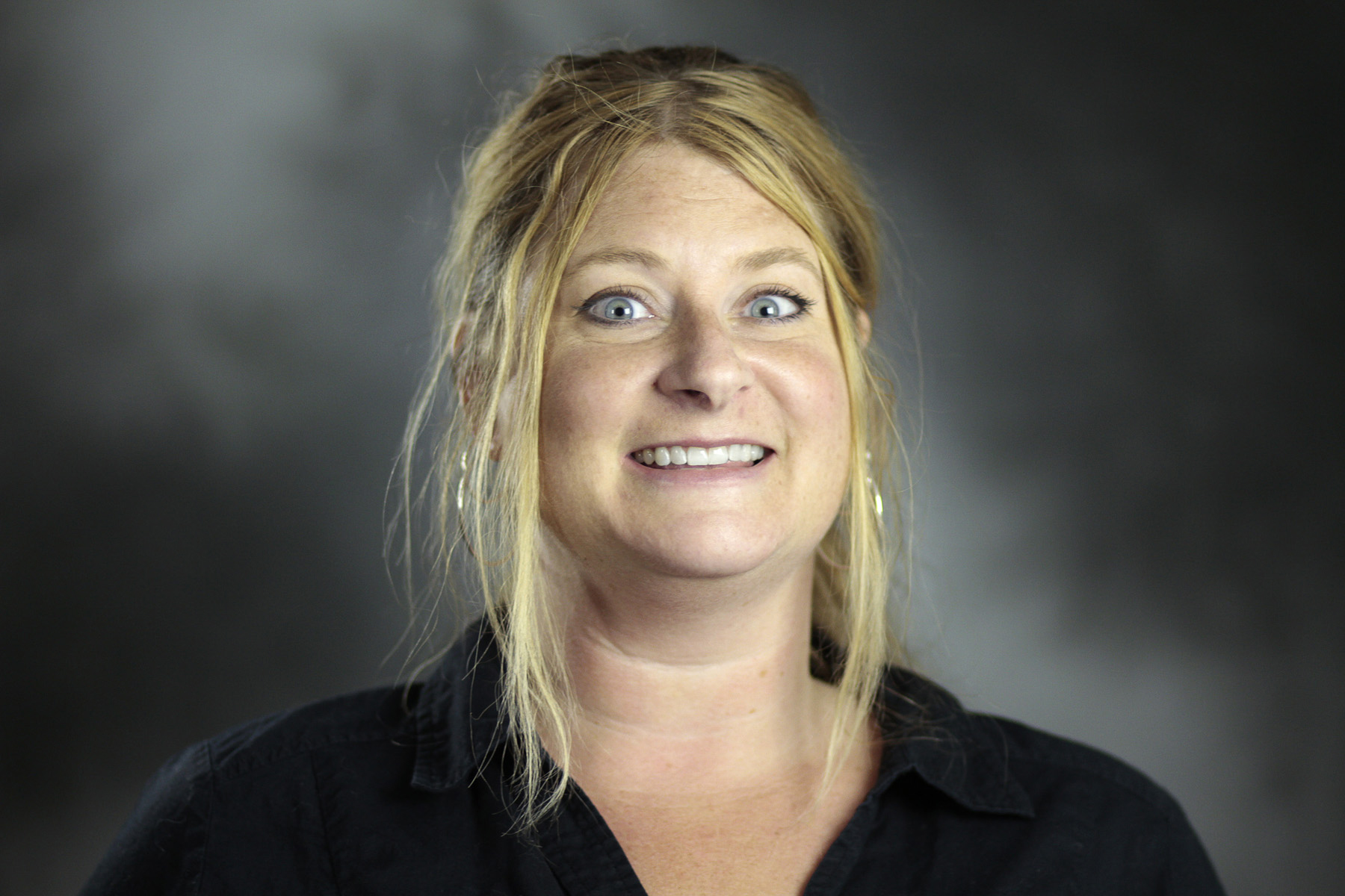 Headshot style portrait of a woman with blonde hair and blue eyes smiling with a black button down shirt.